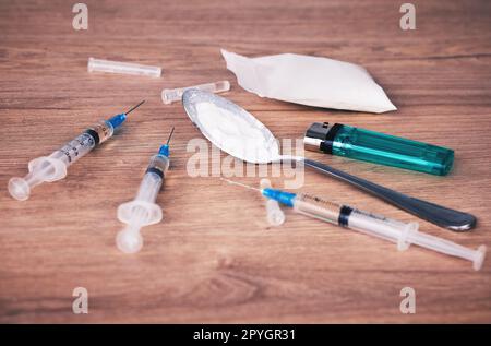 Powder, syringe and drugs with spoon on table for alcohol addiction, drug rehabilitation and narcotics abuse. Medicine, illegal drug and addict problem for meth, cocaine and heroin solution on desk Stock Photo