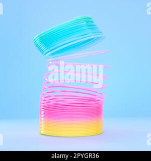 Rainbow slinky toy, spring and plastic product in studio isolated against a blue background mockup. Flexible toys, colorful spirals and childhood item stretched out for playing, having fun and games. Stock Photo