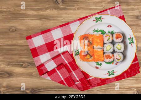 Traditional japanese sushi menu. Various kinds of sushi rolls with salmon, sashimi served on a colorful plate on red checkered napkin on rustic table. Top view. Space. Stock Photo