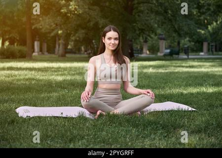 Yoga class in a public park on a warm summer day. A young woman in a lotus position. Stock Photo