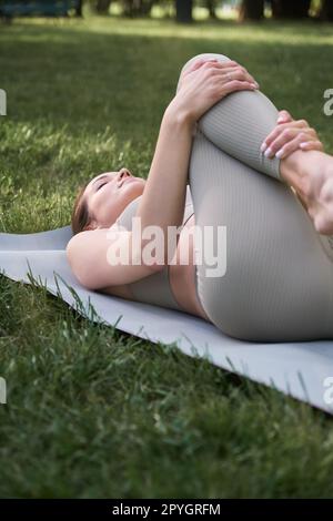 A beautiful slender woman in a gymnastic suit is engaged in yoga or sports, lying on a mat. Stock Photo
