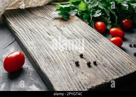 Textured cutting board on gray concrete surface with cherry tomatoes, parsley and peppercorns, cooking food concept Stock Photo