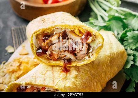 Crispy shawarma with chips, barbeque sauce, chicken in pita bread on wooden dark surface with cherry tomatoes, parsley Stock Photo