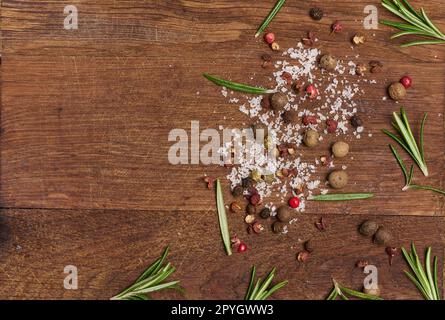 Sprigs and leaves of rosemary, a mixture of peppers and salt on a wooden background, top view Stock Photo