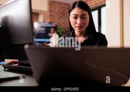 Asian tech enginner analyzing compiling html code on computer display, working on interface development. Software developer using terminal window with firewall server data in it big data agency Stock Photo