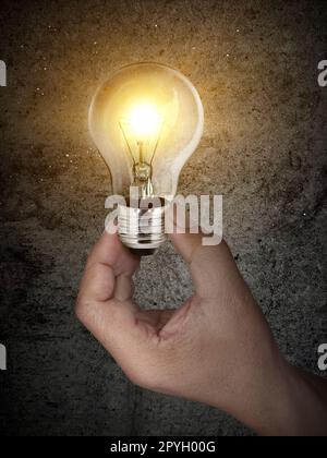 concept creativity with Hand holding glowing light bulb that shine glitter on Concrete floor background Stock Photo