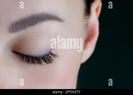 Close-up of closed eye with amazing long eyelashes, black eyeliner, perfect skin, eyebrow of unrecognizable young woman. Stock Photo