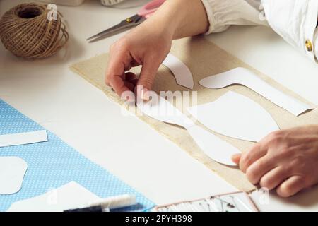 Unrecognizable closeup women, seamstresses holding and placing paper sew pattern, templates on textile sheet in workshop Stock Photo