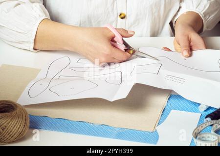 Handcrafted do it yourself tutorial. Cropped female tailor hands cutting out different shapes, patterns from paper sheet Stock Photo