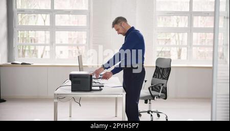 Irritated Businessman Looking At Paper Stuck In Printer Stock Photo