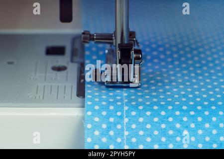 Close up sewing machine steel part with needle, pressure foot stitching with thread on blue fabric, textile. Tailoring Stock Photo