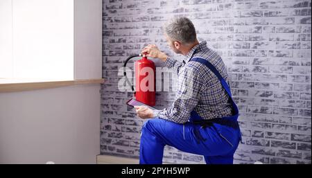 Worker Installing Fire Extinguisher. Inspection Service Stock Photo
