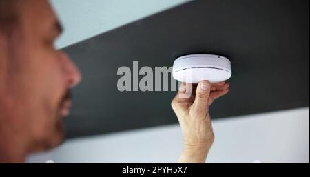 Person's Hand Installing Smoke Detector On Ceiling Wall Stock Photo