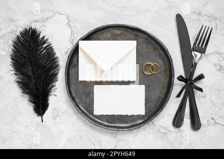 Black wedding table setting with a blank envelope, card and two rings top view, mockup Stock Photo