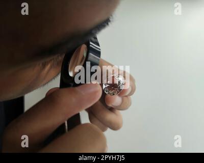 Man jeweller examines polished diamond through magnifier. Buyer checking diamond. Cut and polished diamond. Diamond jewellery under grading. Jeweller looking through loupe Stock Photo