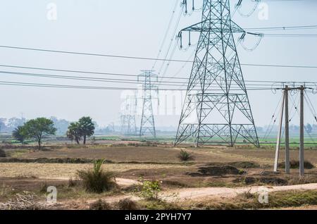 Power lines over an agricultural field against clear sky horizon. High-voltage tower installed in a row on a field. Stock Photo