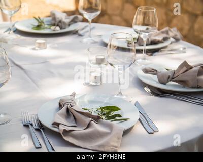 Wedding banquet concept. Chairs and round table for guests, served with cutler and, flowers and crockery and covered with a tablecloth Stock Photo