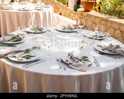 Wedding banquet concept. Chairs and round table for guests, served with cutler and, flowers and crockery and covered with a tablecloth Stock Photo