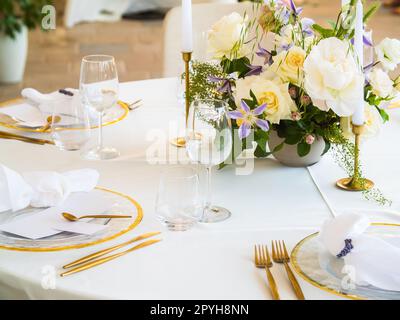 Wedding banquet concept. Chairs and round table for guests, served with cutler and, flowers and crockery and covered with a tablecloth Stock Photo