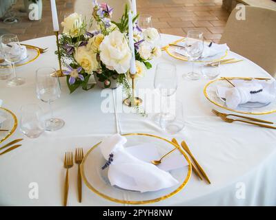 Wedding banquet concept. Chairs and round table for guests, served with cutler and, flowers and crockery and covered with a tablecloth Stock Photo