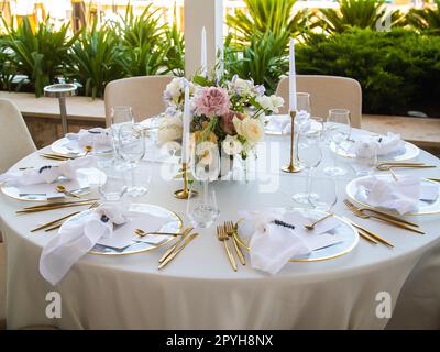 Wedding banquet concept. Chairs and round table for guests, served with cutler and, flowers and crockery and covered with a tablecloth Stock Photo