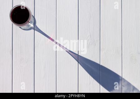 A glass of red wine and its long shadow on a white plank background. Top view. Copy space Stock Photo