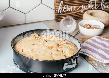 Baking dish with baked apple pie stands on kitchen counter next to ingredients and wooden sign Home sweet home Stock Photo