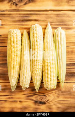 Five sweet yellow raw milk corn cobs maize with green fresh ingredient product. Lie on wooden table. Top view. Close up Stock Photo
