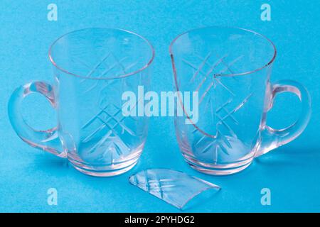 A whole and a broken wine glass with a shard of glass on a blue background. Macro. Stock Photo