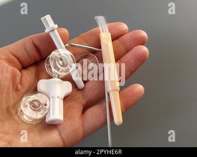 Transparent plastic bobbins from a modern sewing machine in the palm of a woman - seamstresses, needles, thread take-up, whipping tool. Gray background. sewing machines Stock Photo