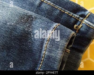 Denim fabric with seams made with red or beige threads close-up. Textile texture. Blue color of the material. Light industry sewing product. Bent and hemmed leg Stock Photo