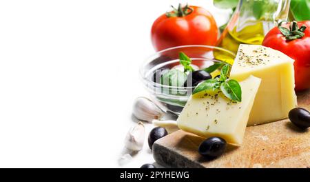 Goat cheese, olives, olive oil, tomato, garlic, basil and spices on wooden cutting board isolated on white background. Food ingredients for italian pizza recipe. Stock Photo