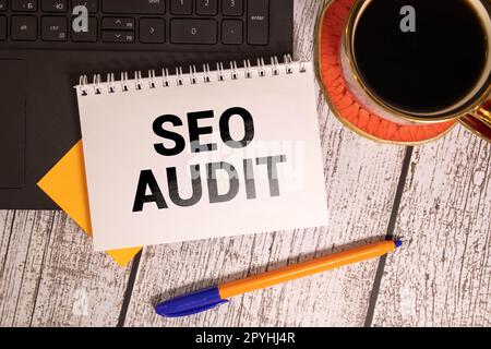 On a light desktop, a pen, yellow paper clips and a white card with the text SEO AUDIT on a yellow background. Stock Photo