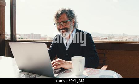 Happy middle aged man communicates remotely using laptop. Working from home office Stock Photo