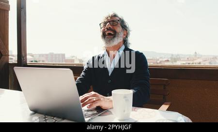 Happy middle aged man communicates remotely using laptop. Working from home office Stock Photo