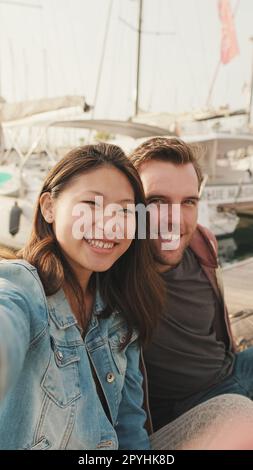 Romantic couple sits on the pier on the yacht background and take a selfie Stock Photo