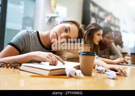 I cant college today. Please dont make me college. Portrait of a young woman looking tired while studying in a college library. Stock Photo