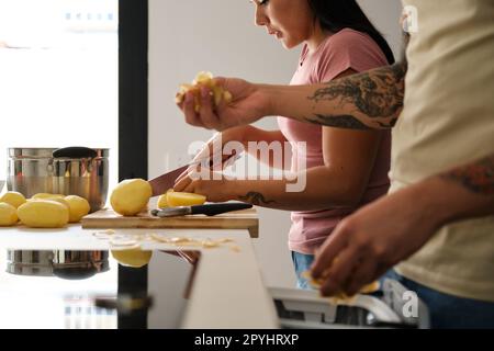 Two young latin people peeling and cutting potatoes at kitchen. Stock Photo