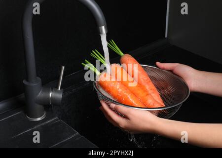Woman washing fresh ripe juicy carrots under tap water in sink, closeup Stock Photo