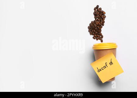 Note with word Decaf attached to takeaway cup and coffee beans on white background, flat lay. Space for text Stock Photo