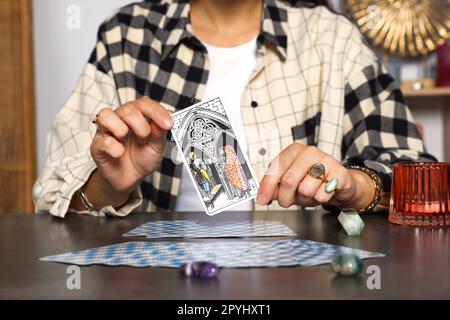 Fortune teller with tarot card Three of Pentacles at grey table indoors, closeup Stock Photo