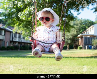 Cute caucasian baby girl toddler on a swing wearing red sunglasses Stock Photo