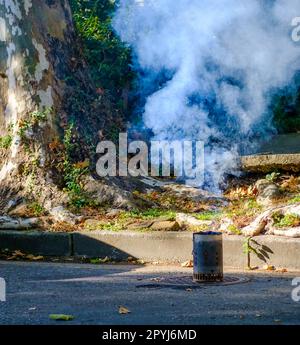 Chimney charcoal starter, with fire and smoke, left on a manhole cover on St. Charles Avenue in New Orleans, Louisiana, USA Stock Photo
