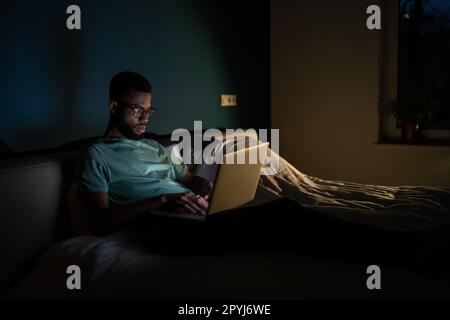 Black guy freelance IT developer using laptop at night, coding until late hours to meet deadline Stock Photo