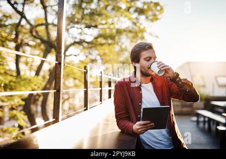 Coffee and connectivity. a handsome young man using his digital tablet while drinking coffee outside. Stock Photo