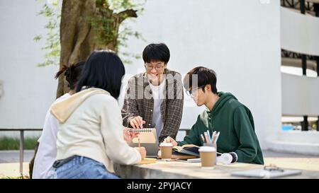 Smart and handsome young Asian male college student is tutoring math to his friends at a campus park on the weekend. Stock Photo