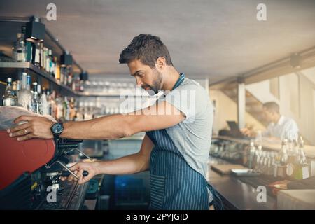 Coffee is his craft. a young man operating the coffee machine at a cafe. Stock Photo