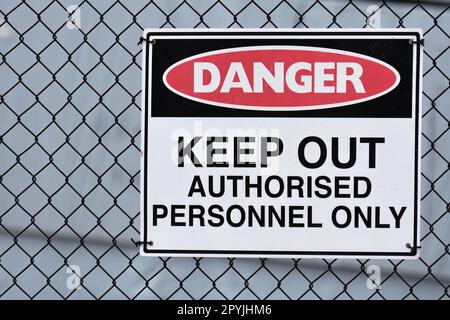 A Danger, Keep out, Authorised personnel only sign on a black wire fence on a light grey background with copy space to the left Stock Photo