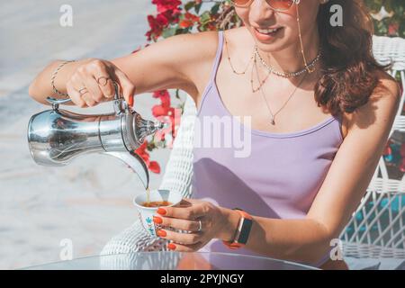 Tourist girl pouring fresh coffee from traditional arabic dallah coffeepot in small cup in authentic cafe in old town of Dubai Stock Photo