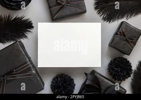 Blank card between Wrapped Gift Boxes, black paper flowers and feathers, mockup Stock Photo